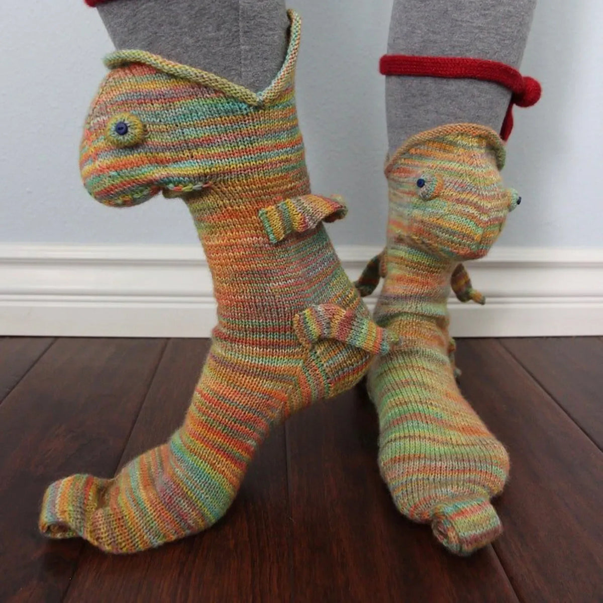 A pair of knitted socks shaped like a crocodile, featuring striped orange and green yarn.