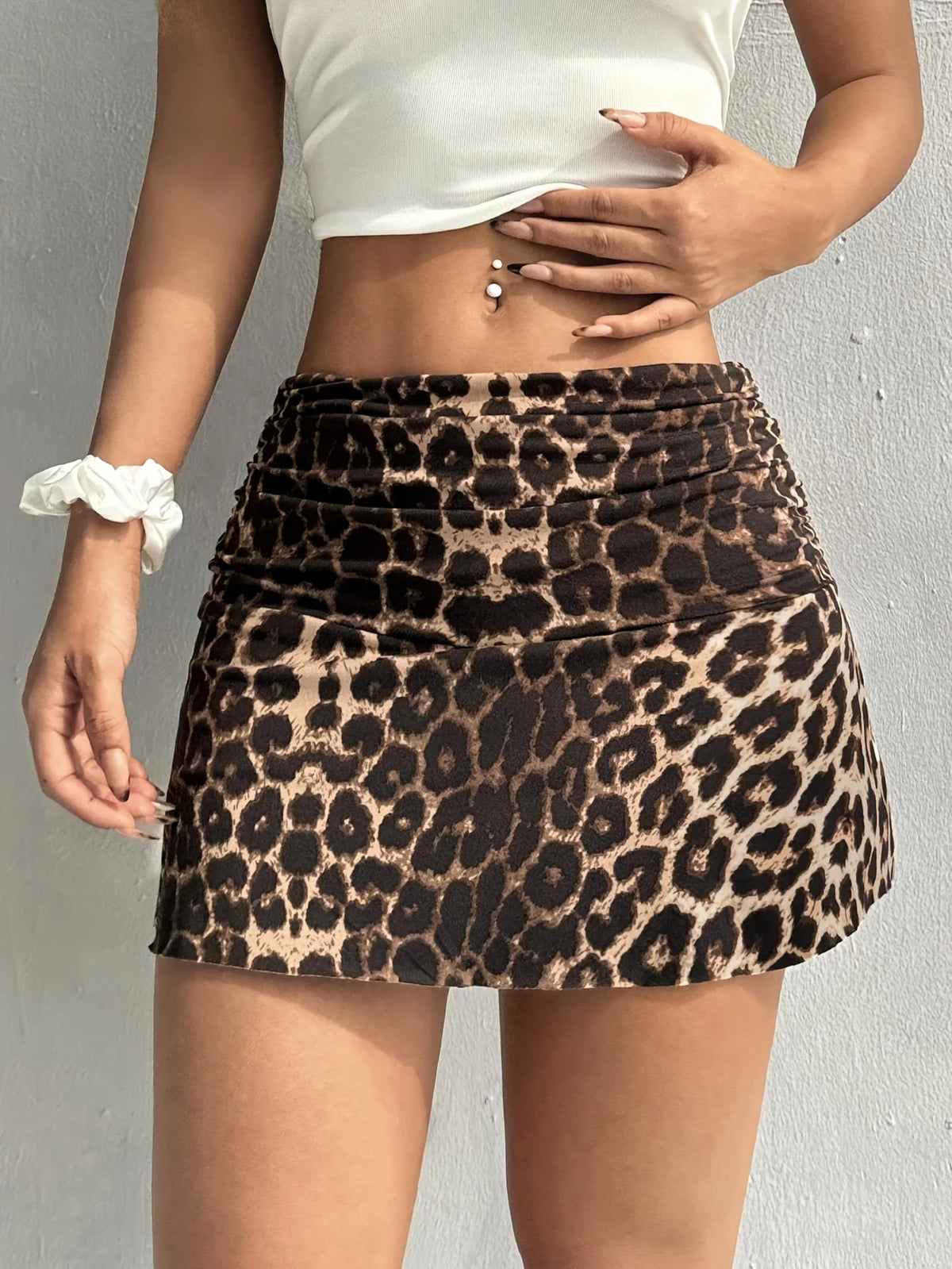 A woman wearing a black and tan leopard print casual mini skirt and a white crop top.