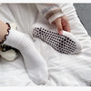A hand is wearing white embroidered yoga socks on a white surface.