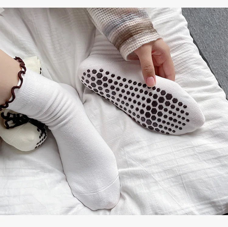 A hand is wearing white embroidered yoga socks on a white surface.