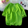 Helles limettengrünes, oversized Baumwoll-T-Shirt einer Frau auf einer weißen flauschigen Oberfläche.