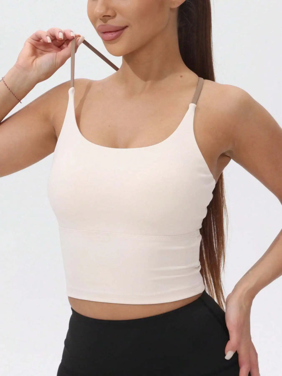 A model wearing a beige women's athletic crisscross tank top and black bottoms.