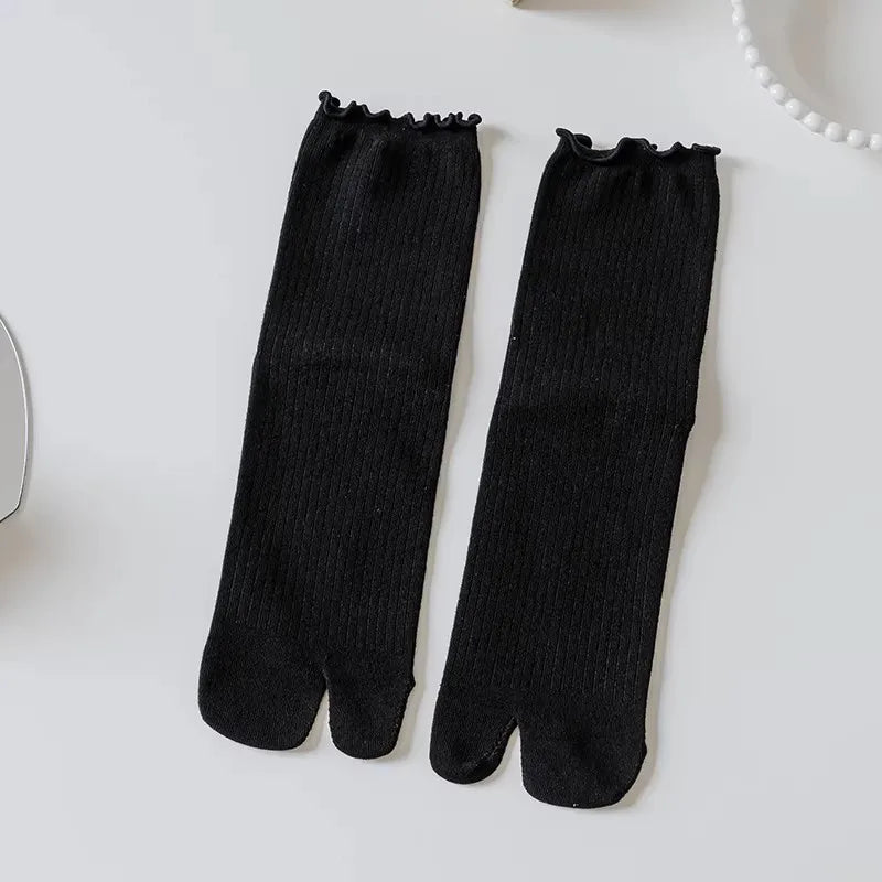 Black knit crew socks with ruffle cuffs displayed on a white surface.