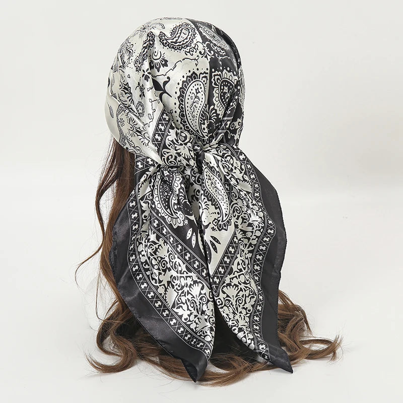 A black and white paisley satin square scarf tied around a person's hair.