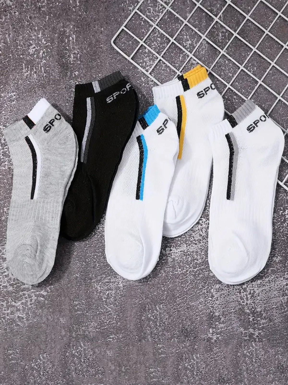A collection of men's color-block mesh ankle socks in gray, black, white, and yellow are displayed on a wire rack.
