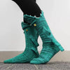 A pair of teal knit crocodile-patterned socks worn on a person's foot.