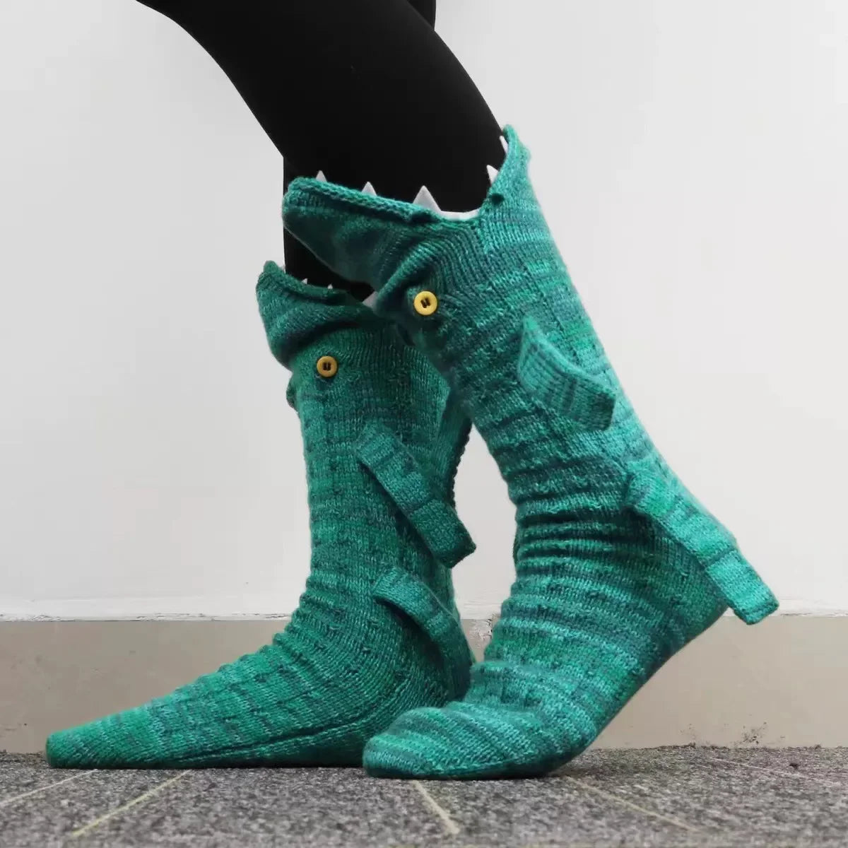 A pair of teal knit crocodile-patterned socks worn on a person's foot.