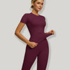 Model trägt ein sportliches Yoga-Set in tiefem Pflaum, mit kurzärmeligem Oberteil und figurbetonten Hosen.