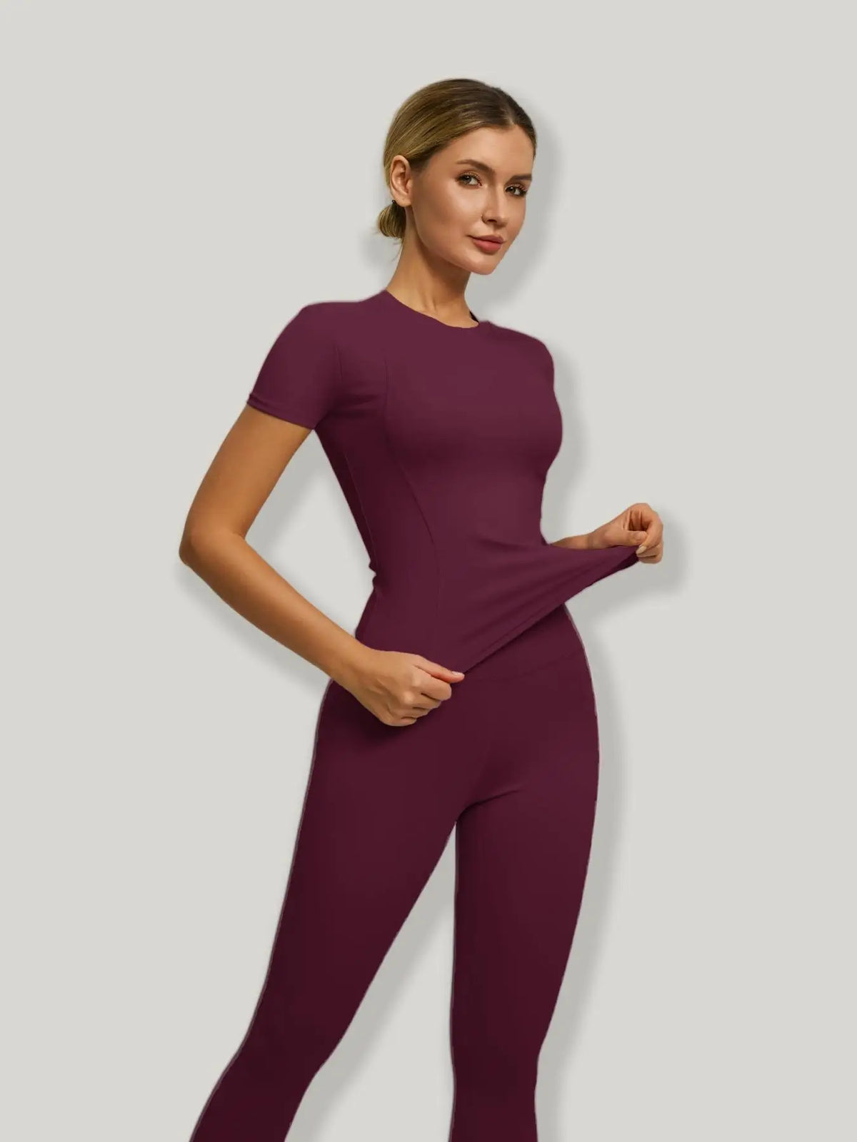 Model trägt ein sportliches Yoga-Set in tiefem Pflaum, mit kurzärmeligem Oberteil und figurbetonten Hosen.