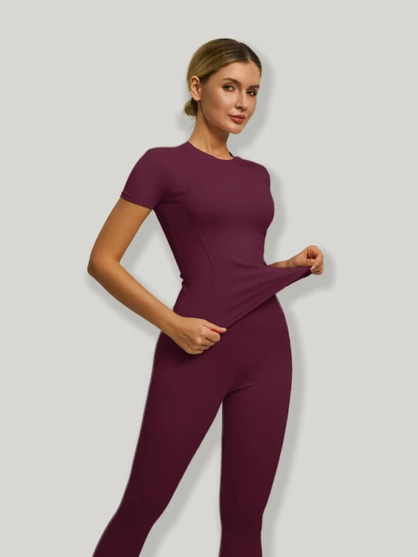 A model wearing a deep plum high-waist sporty yoga set, featuring a short-sleeved top and fitted pants.