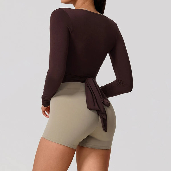 Una mujer vistiendo una blusa de manga larga marrón oscura y pantalones cortos color caqui claro.