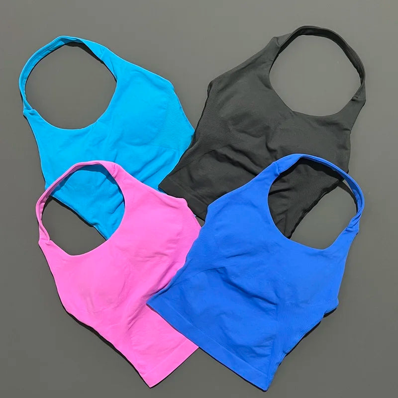 Vier nahtlose Strick-Gym-Tanktops in leuchtendem Blau, Pink und Grau vor grauem Hintergrund.