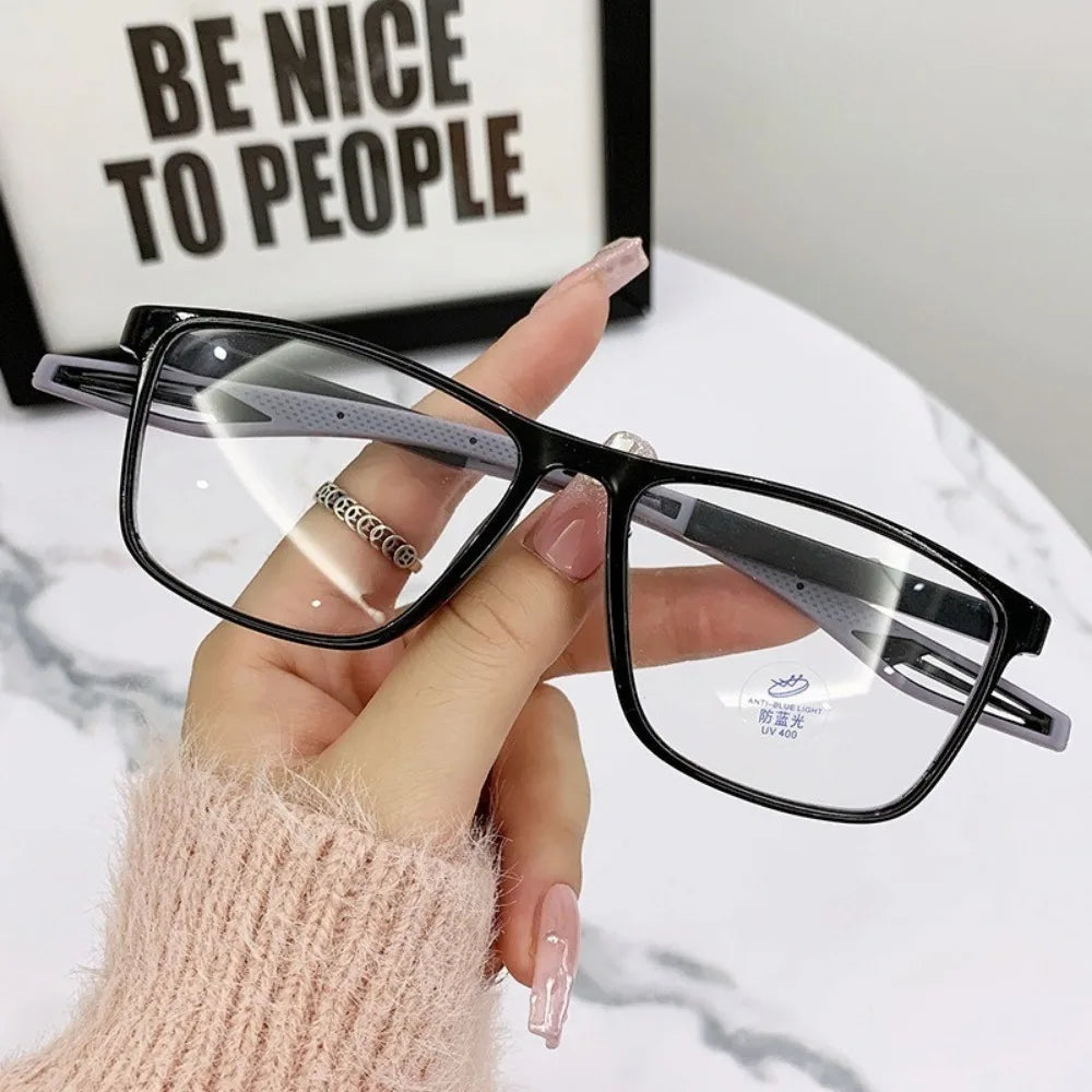 A hand is holding a pair of black-framed sports reading glasses with clear lenses and a pink knitted sleeve in front of a whi