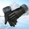 A pair of black ski gloves with gray faux fur cuffs are shown against a snowy outdoor background.