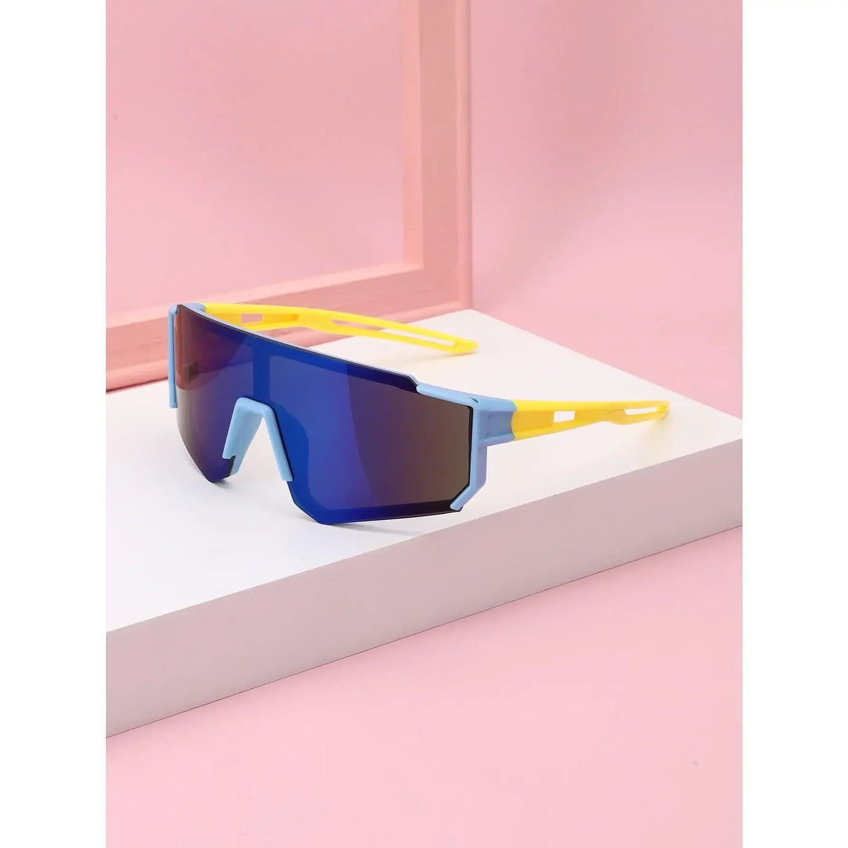 Blue sports sunglasses with yellow arms resting on a white surface against a pink background
