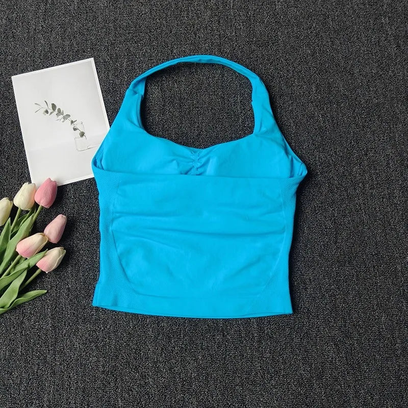 Haut sans bretelles bleu vif pour yoga et fitness, à côté d'une carte blanche et de tulipes roses sur fond gris foncé.