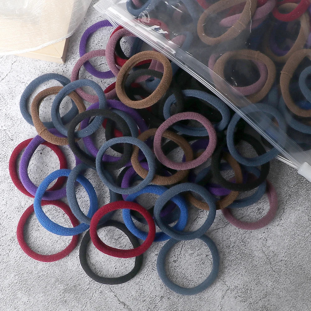 A pile of 50 pieces of mixed color elastic hair bands in various shades of purple, blue, and brown.