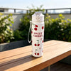 A white insulated tumbler with a silver lid and a design of red cherries on a wooden table.