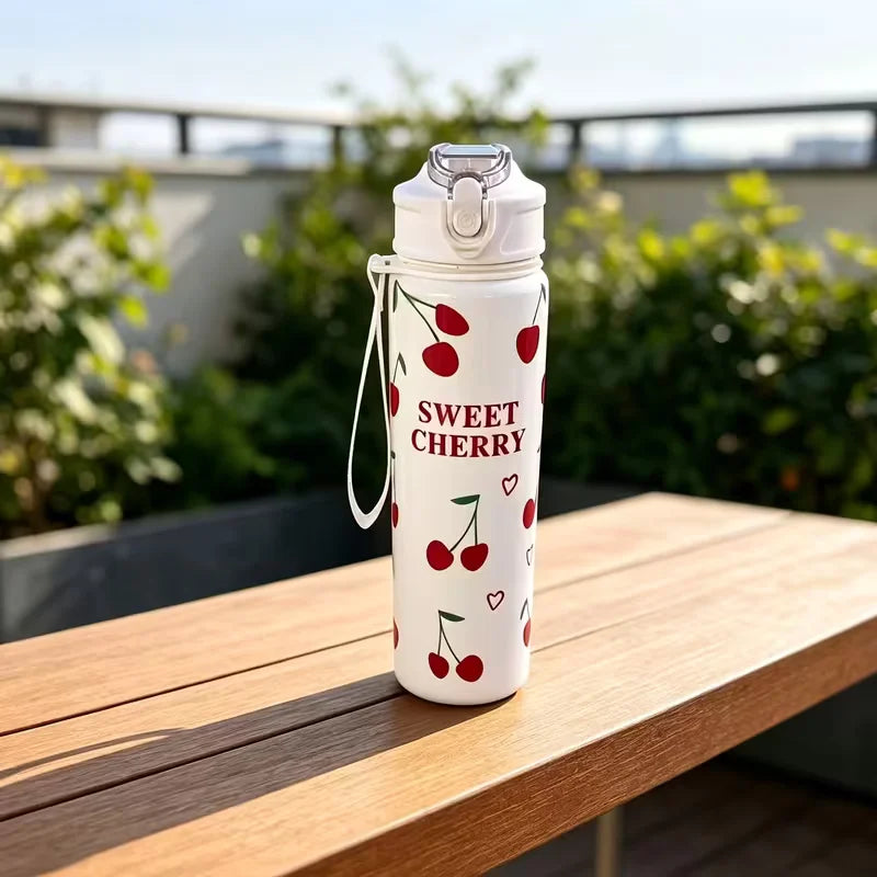 A white insulated tumbler with a silver lid and a design of red cherries on a wooden table.