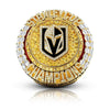A close-up of a gold and diamond championship ring featuring a black stylized letter design.