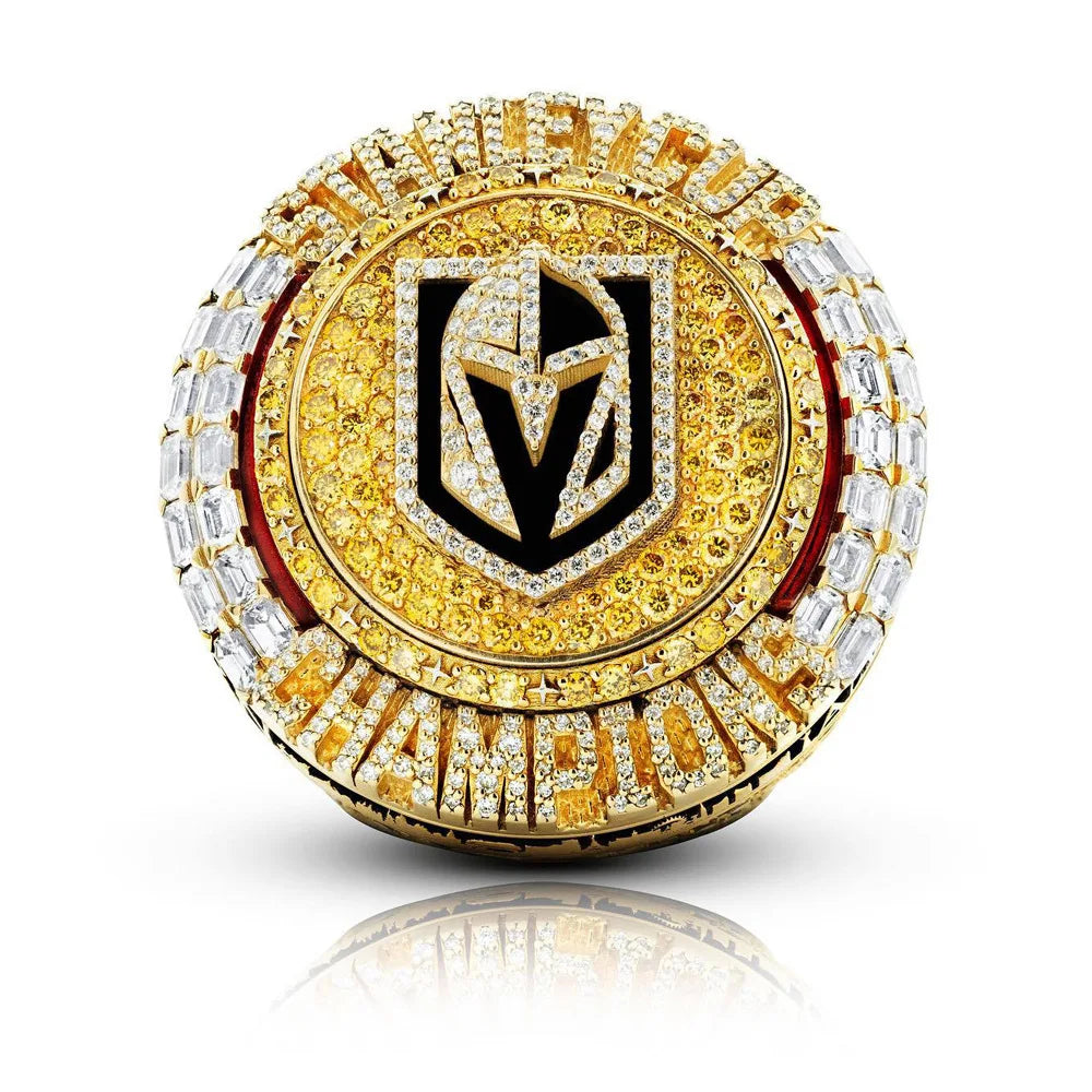 A close-up of a gold and diamond championship ring featuring a black stylized letter design.