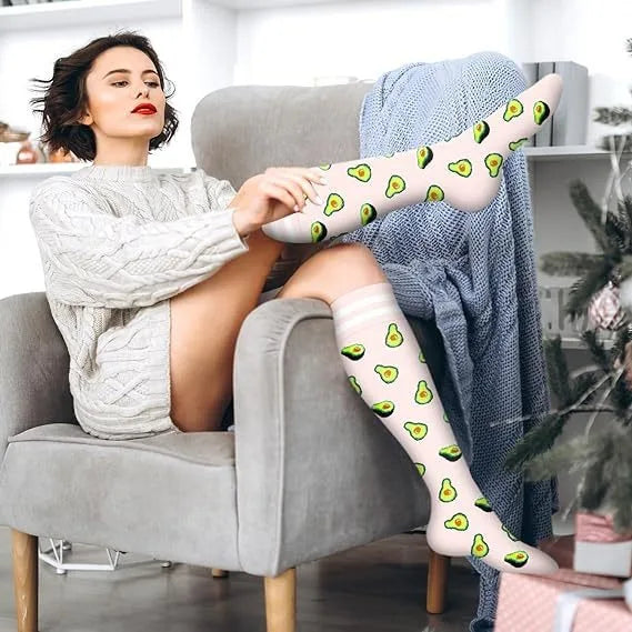 Eine Frau modelliert florale Kompressionsstrümpfe am Fuß, während sie auf einem grauen Sessel sitzt.