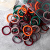 A pile of 50 mixed color elastic hair bands in various shades of orange, green, and red on a gray surface.