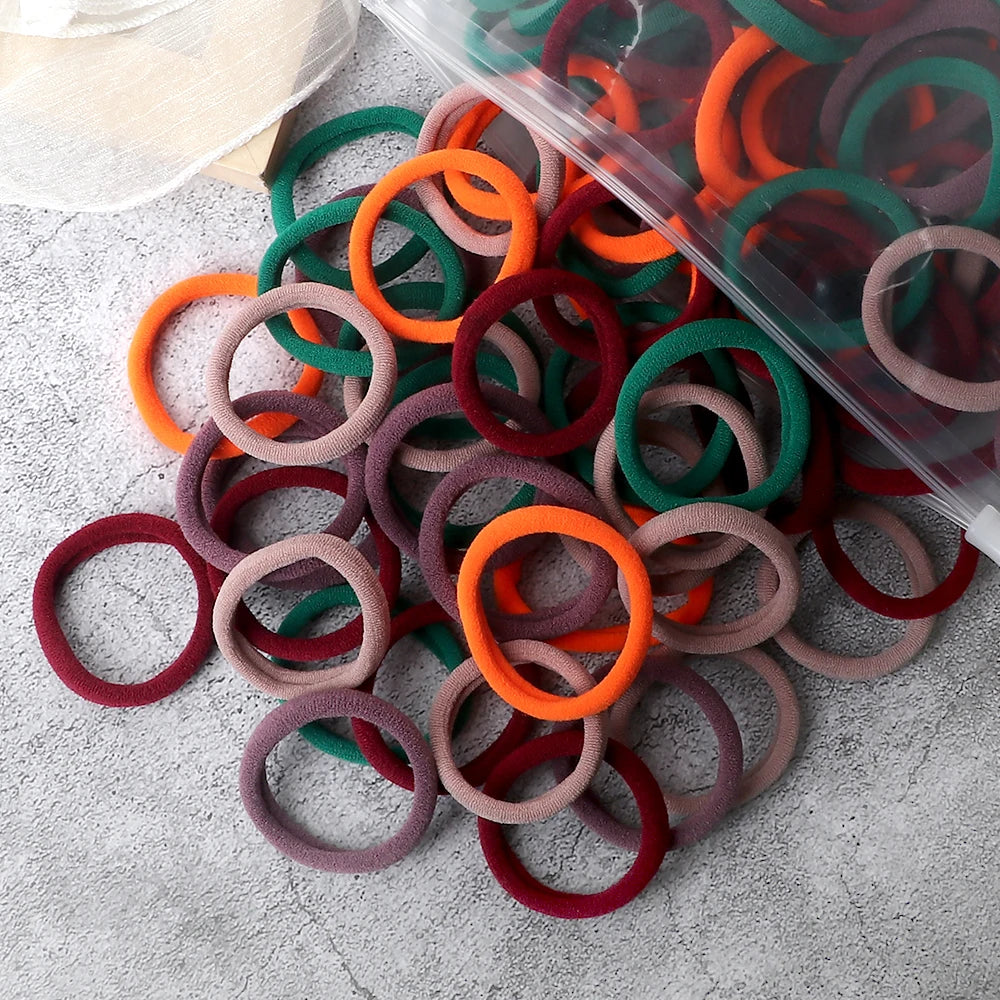 A pile of 50 mixed color elastic hair bands in various shades of orange, green, and red on a gray surface.