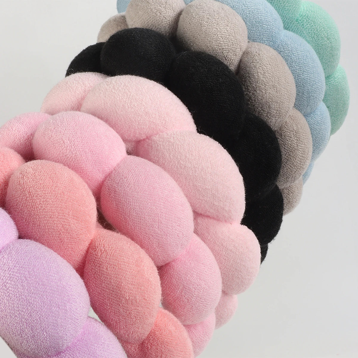 A stack of colorful microfiber skincare headbands and wristbands in shades of pink, purple, black, and mint green.
