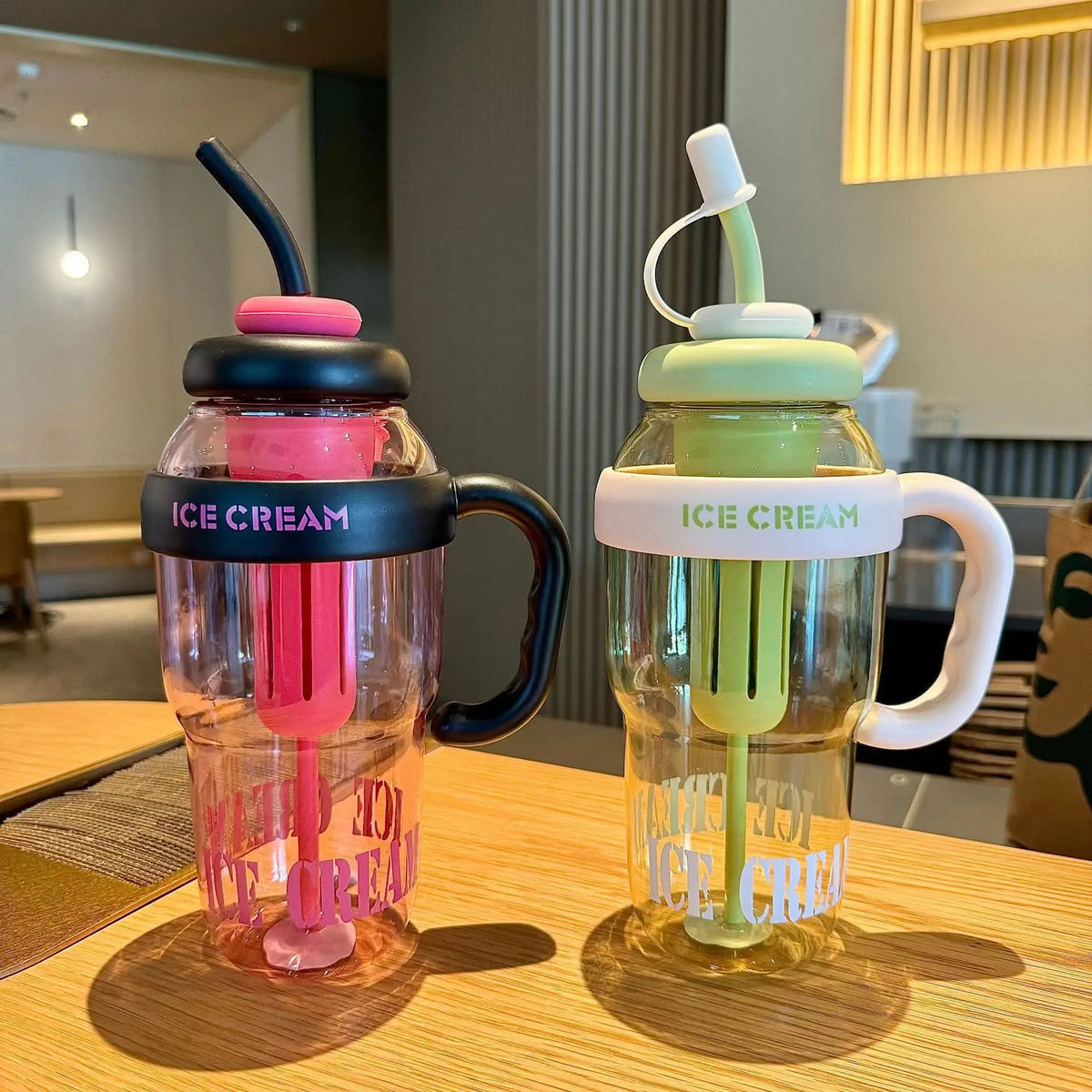 A clear reusable water bottle filled with pink ice cream, featuring a silicone straw and handle.