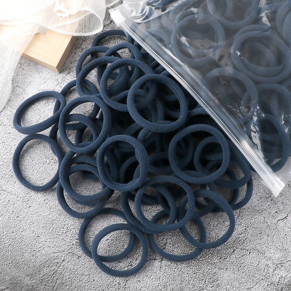 A pile of dark blue elastic hair bands in a clear plastic bag on a gray surface.