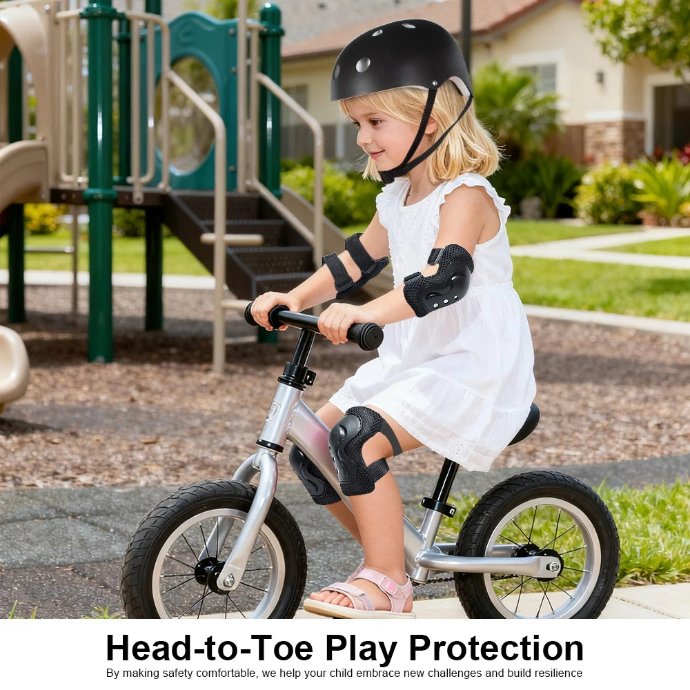 A young girl wearing a black helmet and protective gear is riding a silver bicycle outdoors.