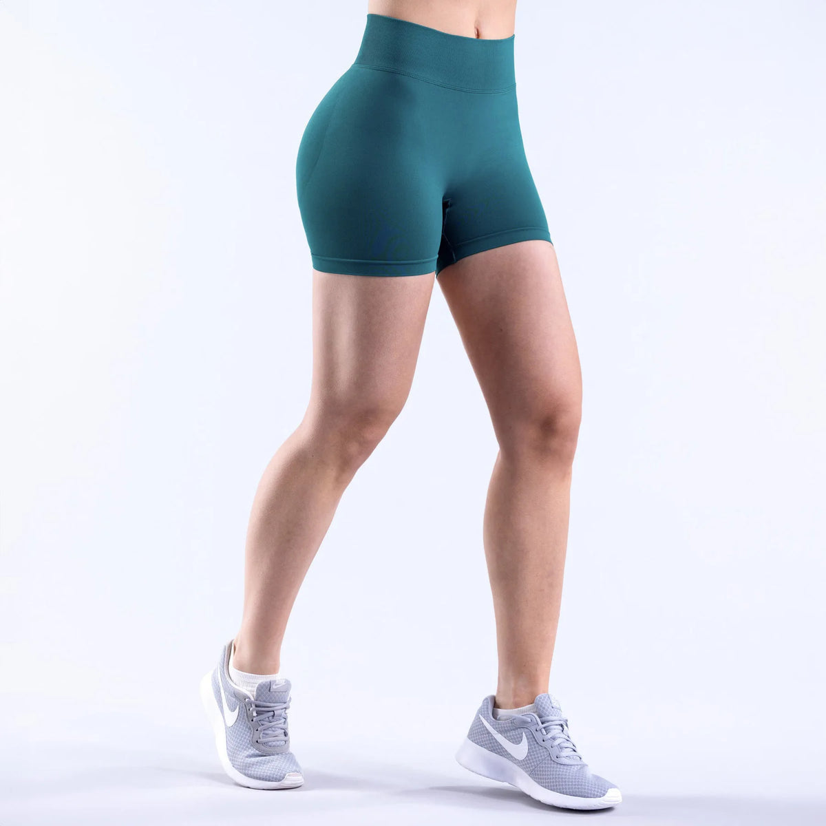 A person wearing teal seamless high-waisted yoga shorts and gray athletic shoes standing against a white background.