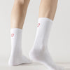 A pair of white crew socks with red heart embroidery worn on a person's legs.