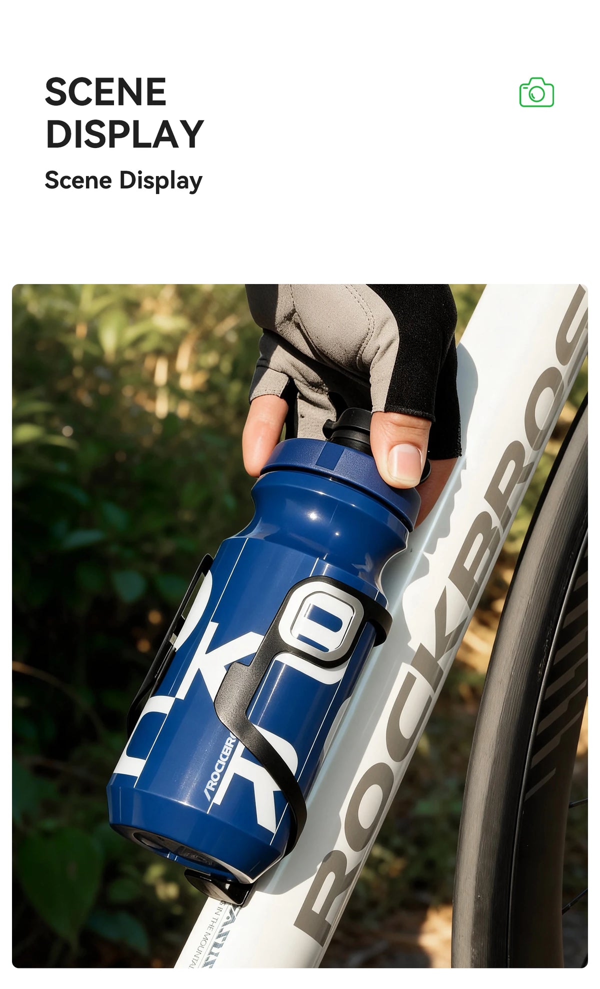 Una botella de agua azul para ciclismo sostenida por una mano, colocada en un cuadro de bicicleta blanca en un entorno exteri