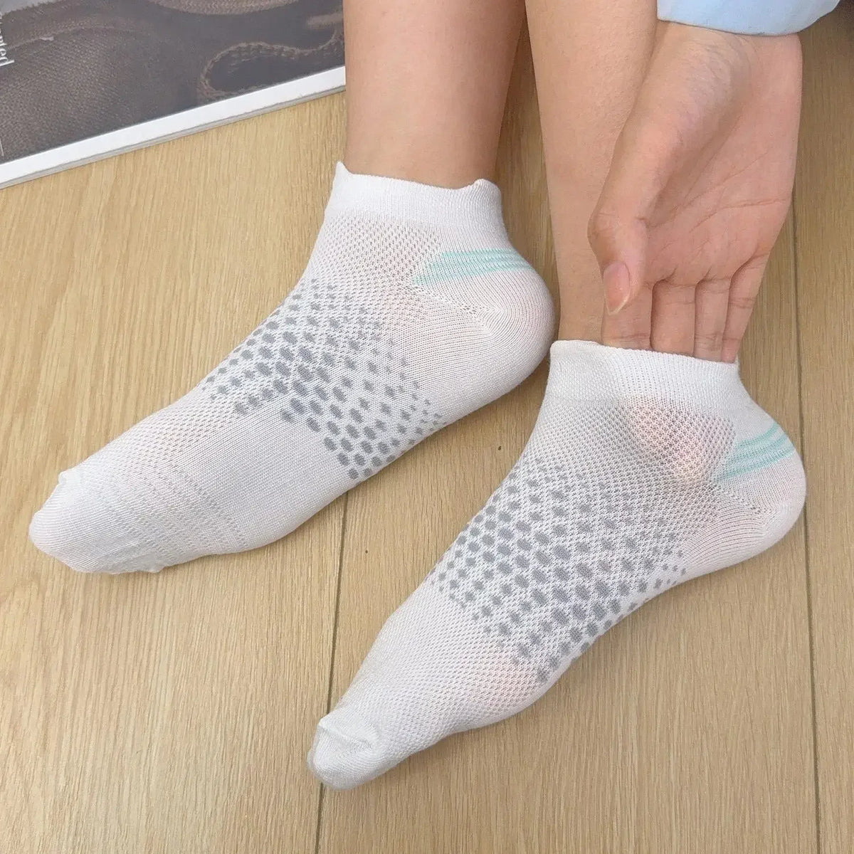 White breathable mesh ankle socks worn on a person's foot against a wooden background.