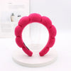 A bright pink sponge terry cloth headband for hair styling displayed on a white stand.