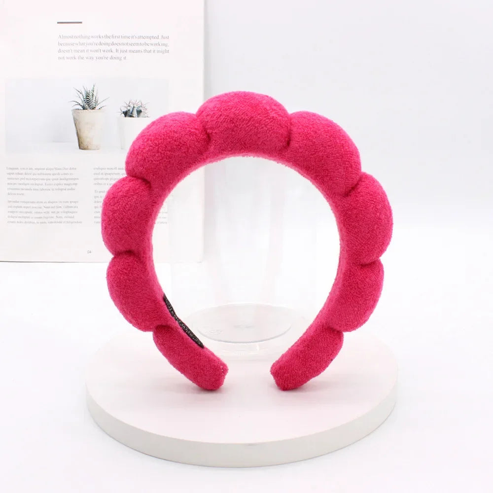 A bright pink sponge terry cloth headband for hair styling displayed on a white stand.