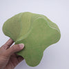 A hand holds a green self-heating lumbar spine patch, showing its contoured shape and textured fabric.