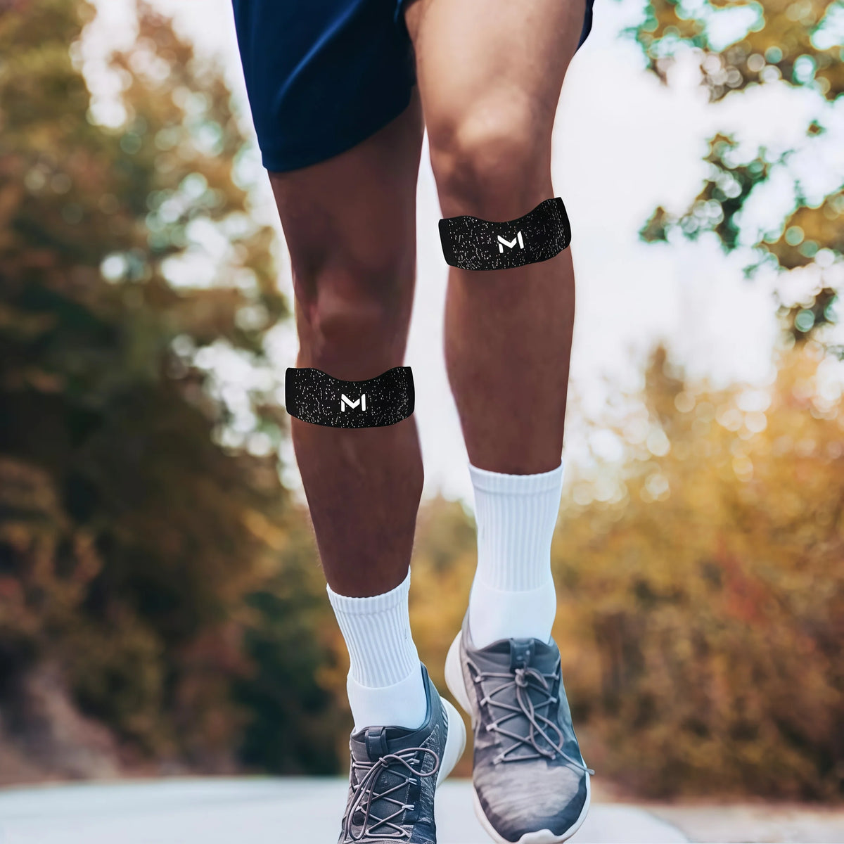 Close-up of a person's legs wearing black knee braces and white socks while running outdoors.