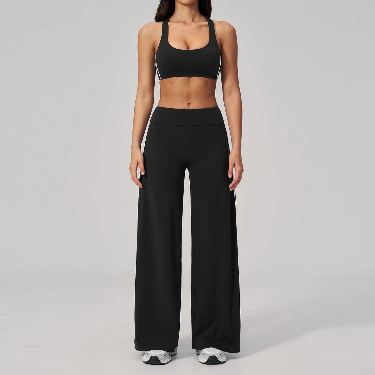 A woman wearing a black two-piece yoga and sports tracksuit set consisting of a cropped top and loose pants.