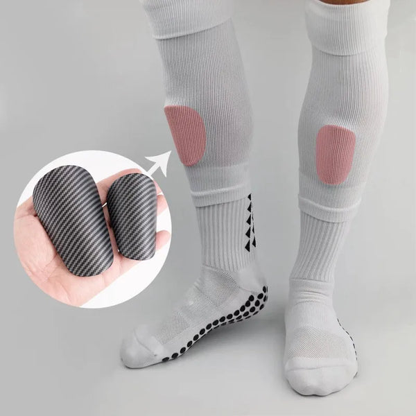 White soccer shin guards with pink accents and black patterned socks shown on a leg.
