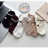 A collection of embroidered yoga socks in various neutral tones, including black, brown, cream, and beige.