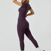 Eine Frau modelliert ein lila Zweiteiler-Yoga-Set mit hohen Bund-Leggings und einem kurzärmeligen Oberteil.