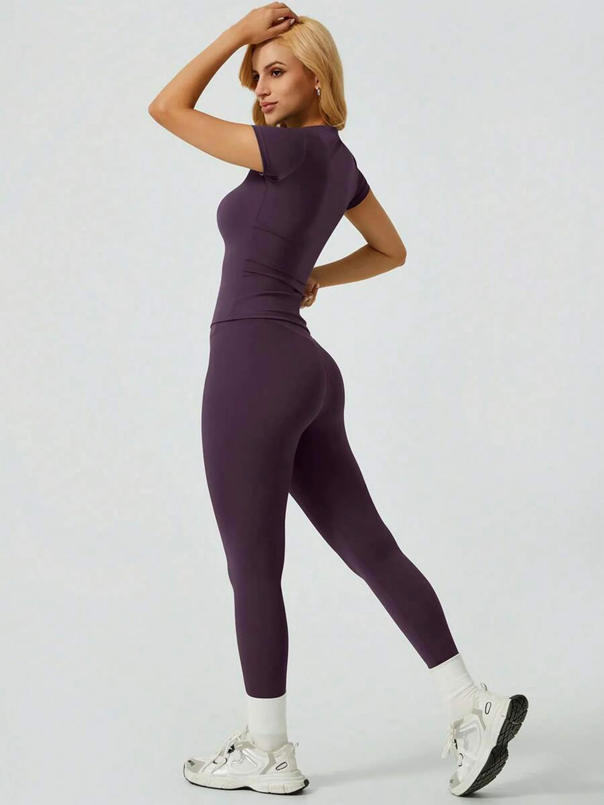 Eine Frau modelliert ein lila Zweiteiler-Yoga-Set mit hohen Bund-Leggings und einem kurzärmeligen Oberteil.
