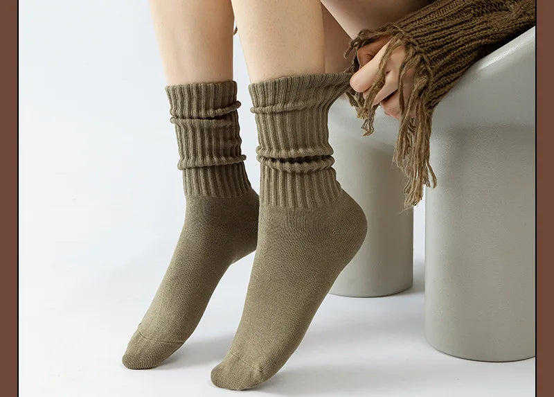 A pair of olive green thick cotton tube socks being pulled onto a person's foot.