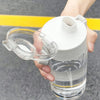 A hand holds a large capacity transparent sports water bottle with a white cap and straw, set against a gray background.