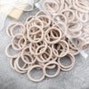A pile of 50 pieces of mixed color elastic hair bands lying on a gray surface.