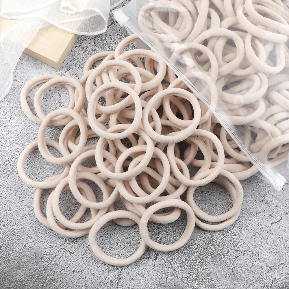 A pile of 50 pieces of mixed color elastic hair bands lying on a gray surface.