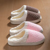 A pair of cozy plush fleece slippers in white and pink are shown resting on a wooden floor.